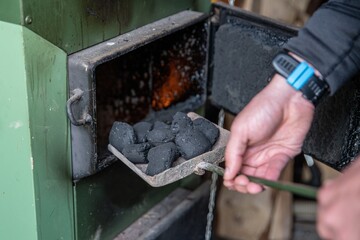 The hands of the man puts the coal into the furnace.