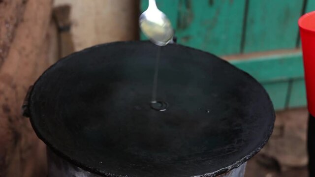 Putting cooking oil on the flying pan from  cap  as it boils as soon as placed on  pan African way of making the Street Role