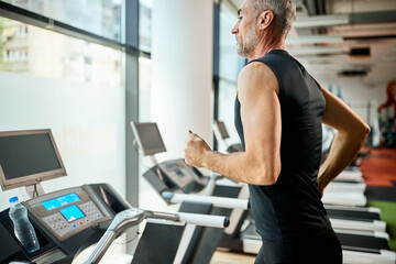 Mature sportsman jogging on treadmill while exercising in a gym.