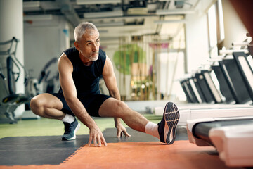 Mature athletic man stretching his leg while working out in a gym.
