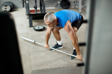 Mature athletic man using barbell while exercising strength in a gym.