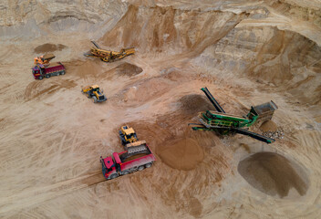 Wheel loader loading sand into dump truck in open pit. Arial view of jaw crusher sand making production line. Heavy mining machinery in quarry. Truck transports minerals from opencast. Soft focus