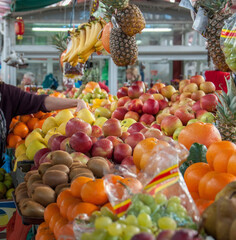 Woman hand choose fruit at fresh fruit produce local market. Counter of street market stall with various fruits, apples, oranges, bananas, pineapples. Authentic market of farming produce