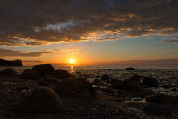 The sea bay and granite boulders in the golden gleam of the sunset under the twilight red-blue sky and beautiful clouds.