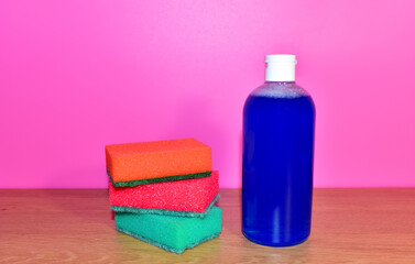 Obraz na płótnie Canvas Detergent bottle and sponges on pink background. Concentrated and anti-bacterial liquids for wash of dirty on tile ceramic. Sponge and detergents and anti-bacterial liquids