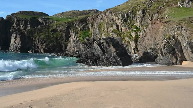 4k slow motion waves crashing on Dail Mor beach on Isle of Lewis, Scotland. Sunny day with blue sky. Sand, rocks, cliff, dramatic crashing wave.