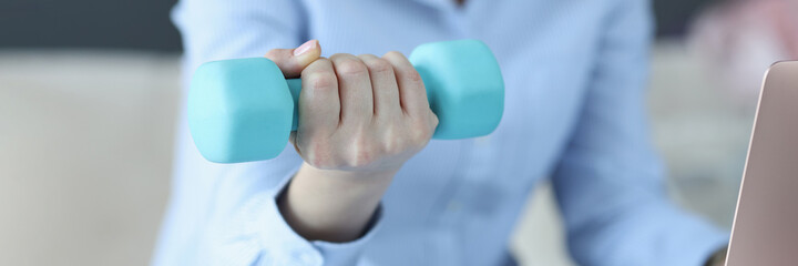 Woman sits on laptop and holds blue dumbbell in her hand