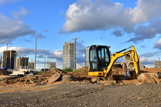 Mini excavator during earthmoving at construction site. Backhoe dig ground for the construction of foundation and laying sewer pipes district heating. Earth-moving heavy equipment on road works