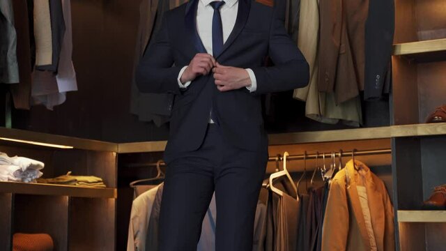 Elegant man trying on a jacket in a shop. In the background classic suits and jackets