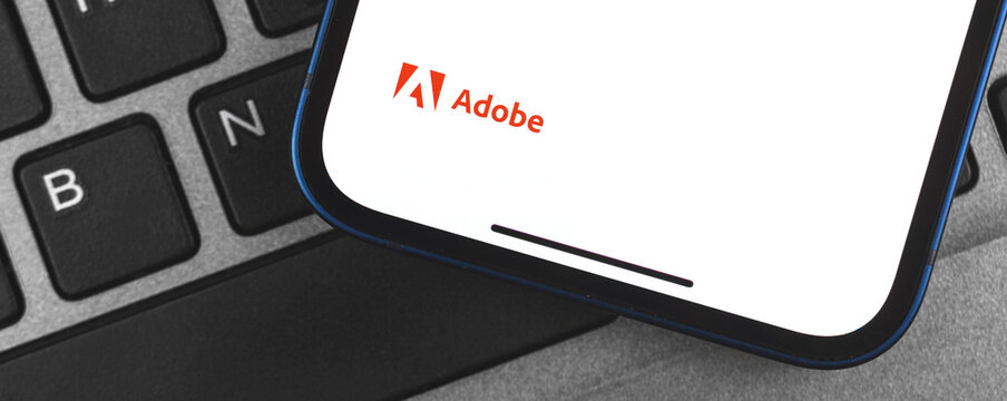 Kharkov, Ukraine - May 28, 2021: Adobe logo banner on the screen of mobile phone, background of laptop keyboard close-up