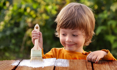 Young boy painting the wooden fence in summer garden
