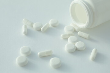 On a white background lies a plastic bottle with medical pills scattered nearby