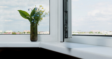 A bouquet of summer flowers on the windowsill of a new plastic window