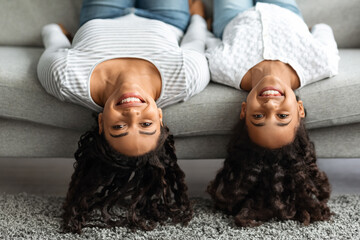 Cheerful mother and daughter laying upside down on couch
