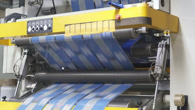 Flexo printing. Film spins between shafts. Printing house. Roller machine prints. Shaft rotates rapidly. Anilox shafts