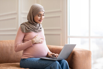 Pregnant Muslim Woman Using Laptop Sitting On Couch At Home