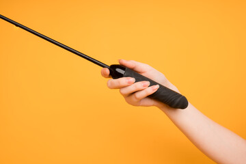Black leather whip in a female hand on an orange background. Sex toys, space for text, useful for a sex shop