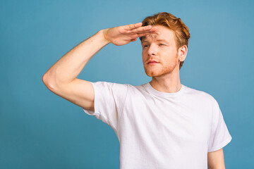 Portrait of a serious young man straring and looking far away isolated on blue background.
