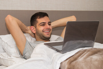 smiling man in bed working with laptop