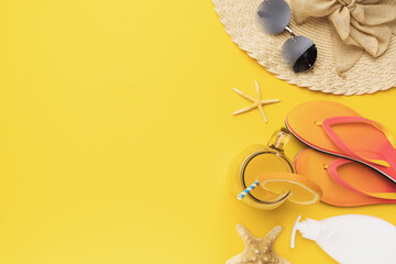 Hat, sunglasses, beach slippers, starfish and orange juice on a yellow background with copy space