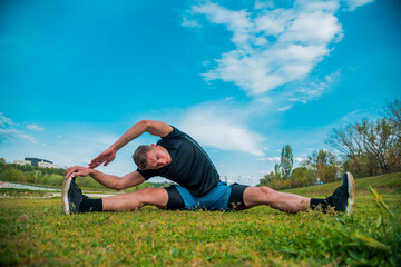 Young sportive man doing exercise before running in morning field outdoors