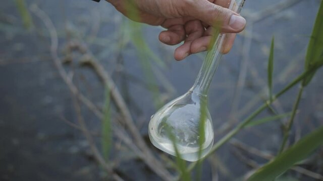 Men's Hand draws water from a polluted reservoir and holding test tube for analyzes with water on the background of the reservoir, the concept of water purity,