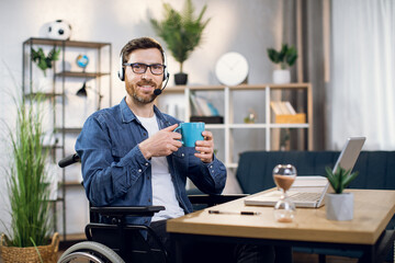 Handicapped male freelancer in eyeglasses and headset having coffee break during working day on...