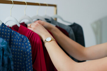 Personal stylist is helping to choose the outfit she goes through hangers with clothes
