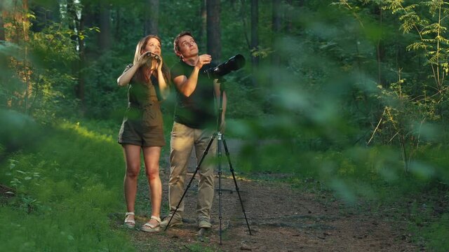Birdwatching in park. Couple watch birds with binoculars and camera with telephoto lens. Amateur birdwatchers spot birds in the spring park