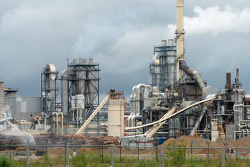 Fototapeta na wymiar Wood processing plant against the background of gray clouds. White toxic smoke comes out of factory chimneys. Utopian landscape. Environmental pollution. An environmental disaster.