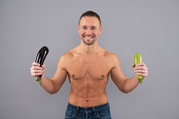 Happy muscular man hold healthy fresh vegetables grey background, mens health and erection.