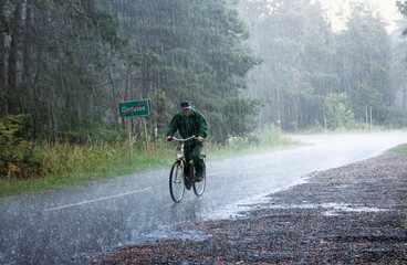 Summer landscape - an elderly cyclist riding a country road in the pouring rain, within Tomaszow Lubelski County, Lublin Voivodeship, in eastern Poland
