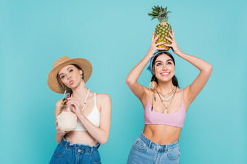 Pretty women holding pineapple and cocktail in coconut isolated on blue.