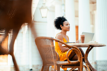 Works on a laptop and tablet, makes an online project on a new design. Freelancer break at the restaurant. A confident stylish woman of African American appearance sits in a summer cafe.