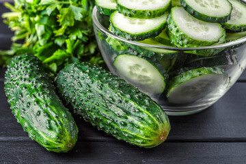 Cucumber on  dark wood texture background.Cucumbers harvest in summer. Cucumbers for salads or canning. Summer vegetables.Slices of fresh cucumbers in a bowl.
