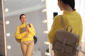 Young woman taking mirror selfie in stylish outfit at home. Morning routine