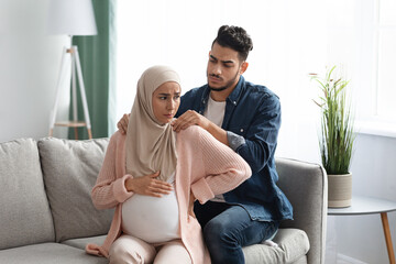 Caring arab husband making neck massage to pregnant muslim wife at home