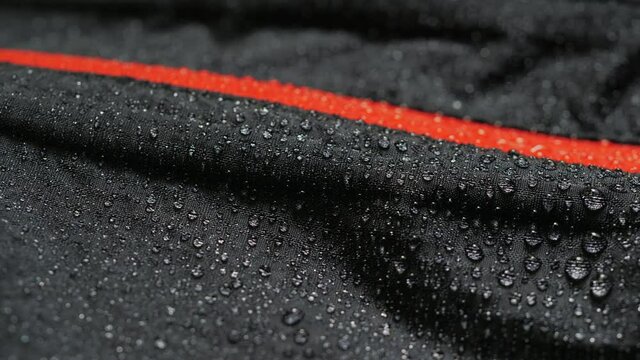 Water droplets on the waterproof fabric. Close-up of a waterproof jacket. Black clothes with red zipper