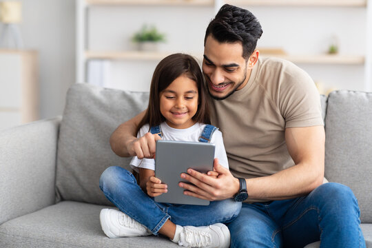 Smiling dad and daughter sitting on couch, using digital tablet