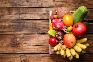 Crate with different exotic fruits on wooden table, top view. Space for text