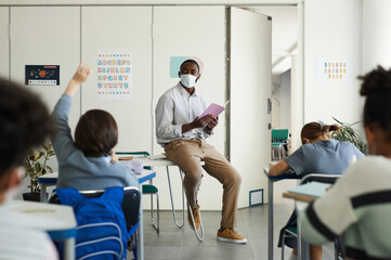 Wide angle portrait of African-American teacher wearing mask in school classroom, covid safety...