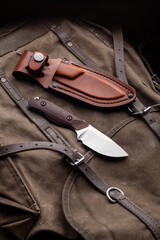 A hunting knife with a wooden handle and a leather case on a khaki canvas backpack. Weapons for self-defense and survival.