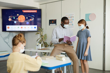 Portrait of kids and teacher wearing masks in school classroom, covid safety measures, copy space