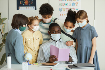 Portrait of diverse group of children and teacher wearing masks in school classroom, covid safety measures