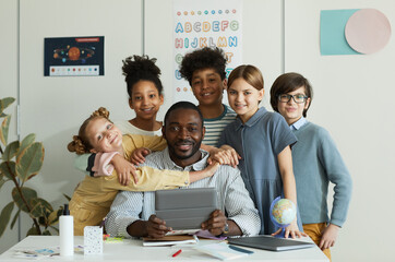Portrait of diverse group of children with male teacher looking at camera in school classroom
