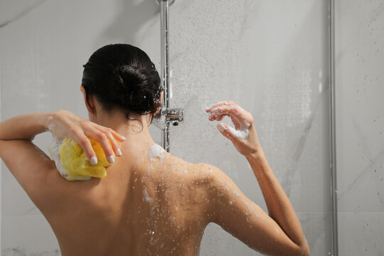 Young Woman With Mesh Pouf Taking Shower At Home, Back View