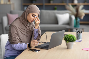 Tired muslim woman sitting at desk, rubbing dry irritated eyes
