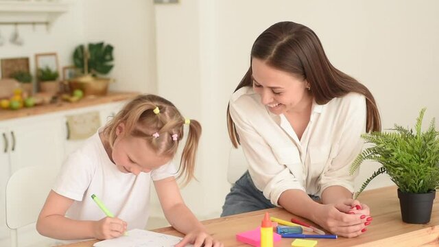Mom and daughter are doing homework. A little girl thoughtfully completes math assignments under the supervision of a tutor. The concept of taking care of a child and helping with homework