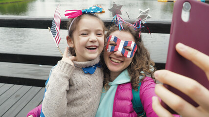 Close up. Cute girl and woman wear symbols usa national flag, happily talk in video conference by smartphone together, celebrating 4th of July. Activity technology lifestyle mobile phone use concept