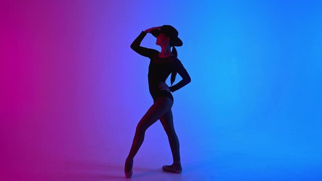 Contemporary ballet dancer woman in hat posing on multi-colored gradient pink blue background. Professional ballerina in sexy costume of femme fatale, solo performance.